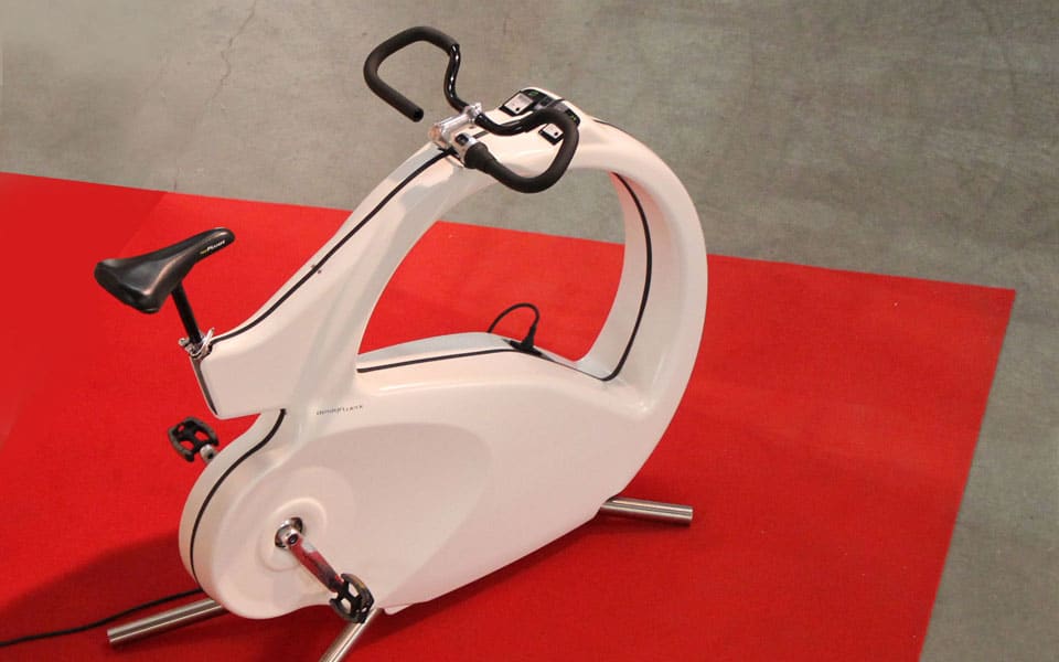 White stationary exercise bike with a curved frame on a red mat, ready for indoor cycling.