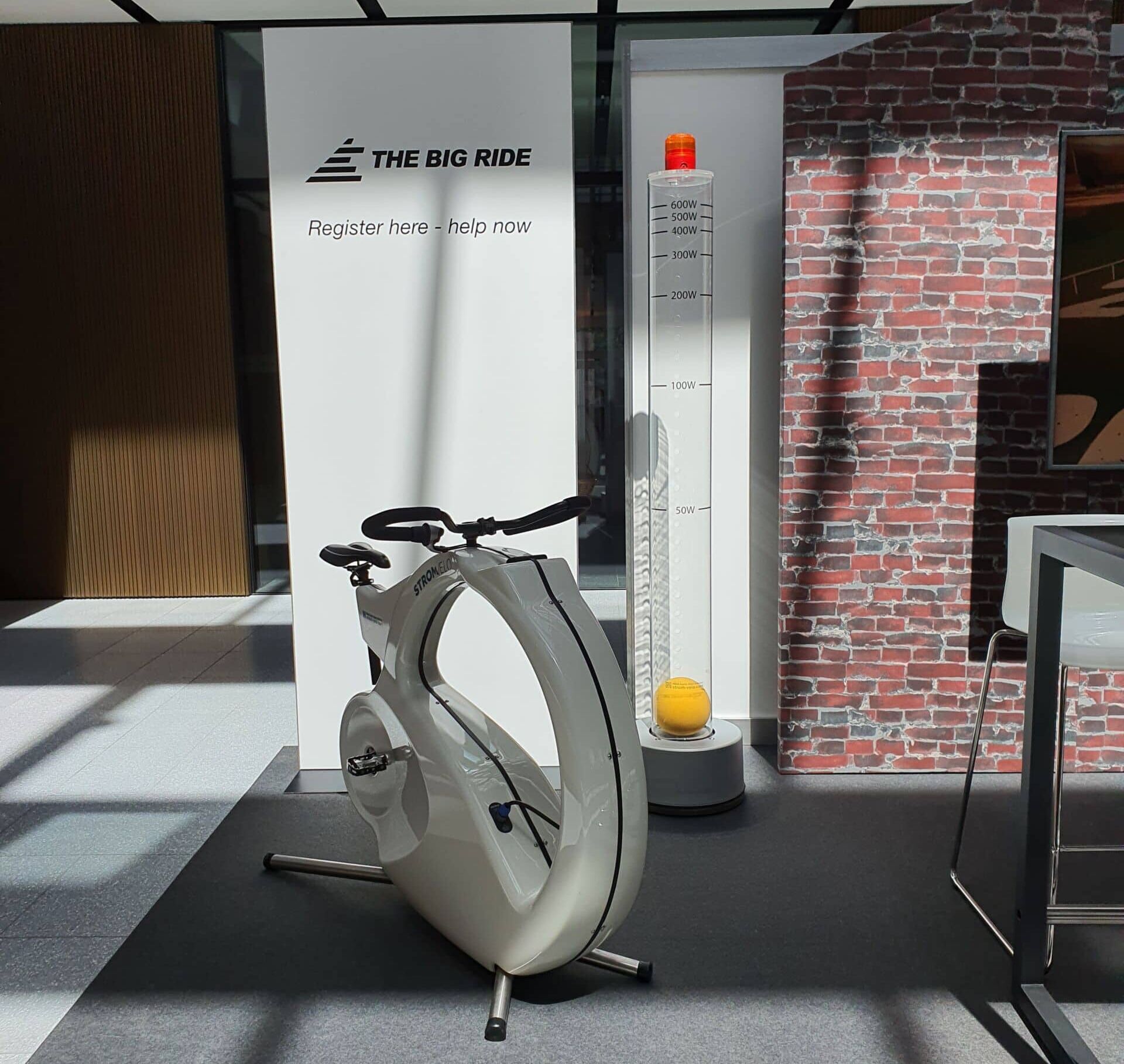 20220510_140641 | Strom-Velo White stationary exercise bike on display in a modern showroom with a tall thermometer prop and brick wall backdrop.
