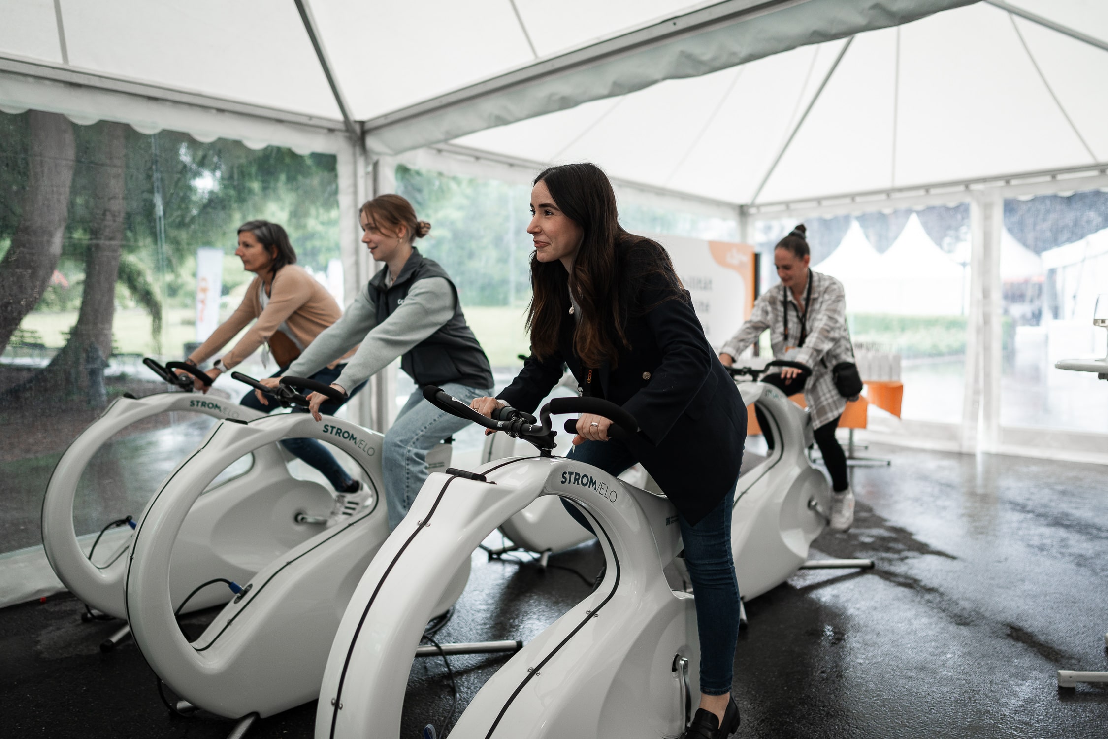 Group of people cycling on stationary bikes inside a bright white tented room, focusing on workout session in progress.